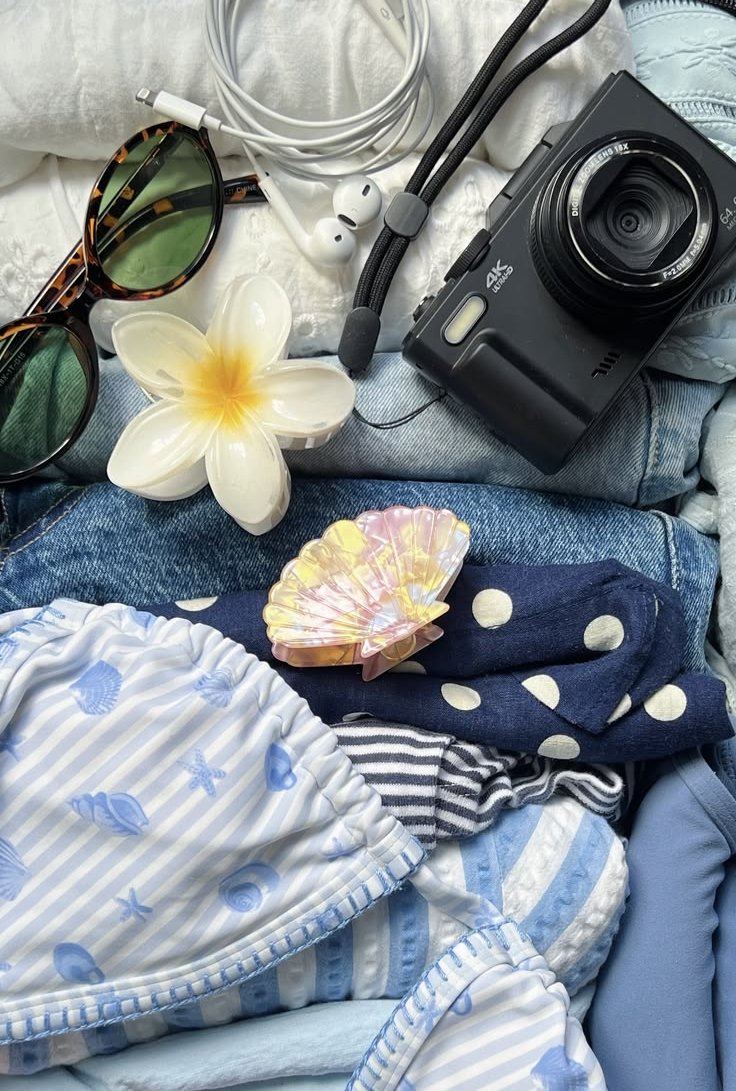 An open pastel-blue suitcase packed for travel with a camera and sunglasses